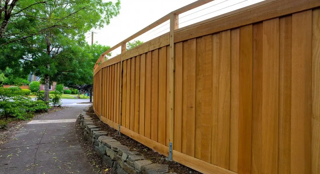 tall wood privacy fence with a modern top rail design along a sidewalk