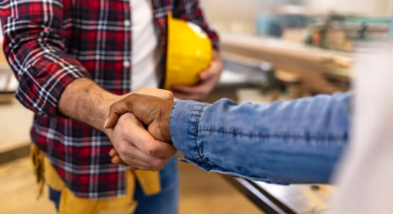 two people shaking hands, one holding a yellow hard hat