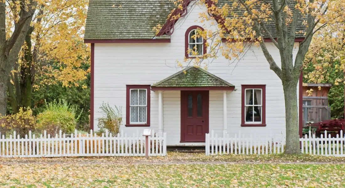 white picket fence in front of a house with autumn trees
