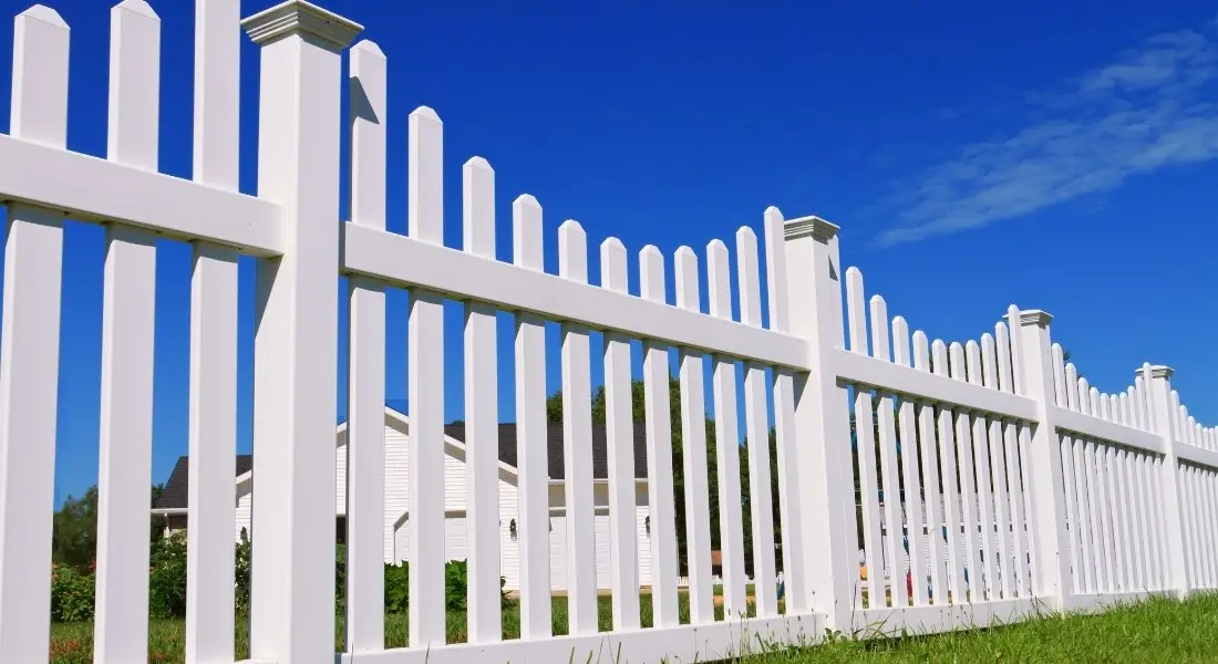 white vinyl picket fence in front of suburban homes under blue sky