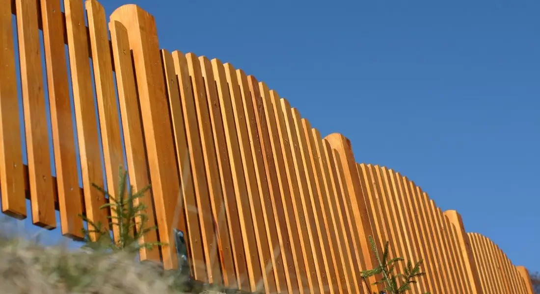 wood fence with decorative scalloped top design against blue sky